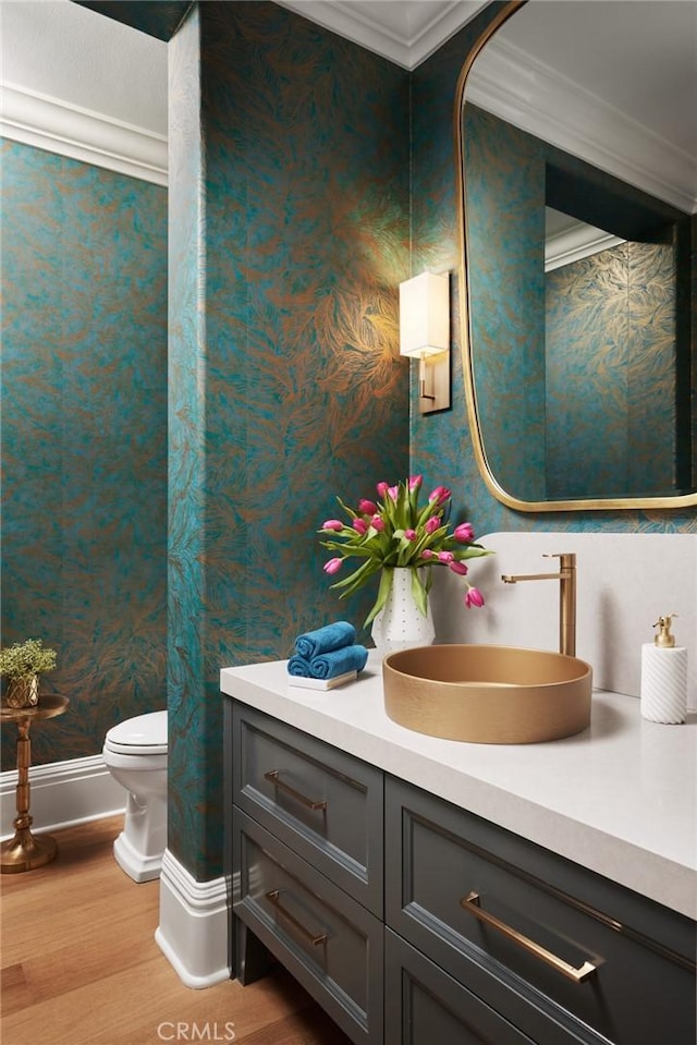 bathroom with toilet, crown molding, vanity, wood finished floors, and wallpapered walls