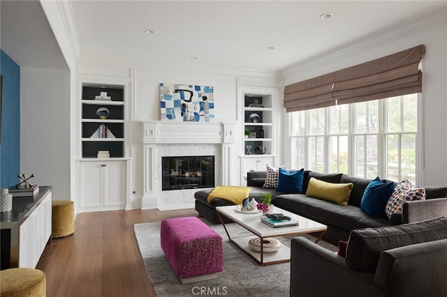living room featuring wood finished floors, ornamental molding, a high end fireplace, and built in shelves