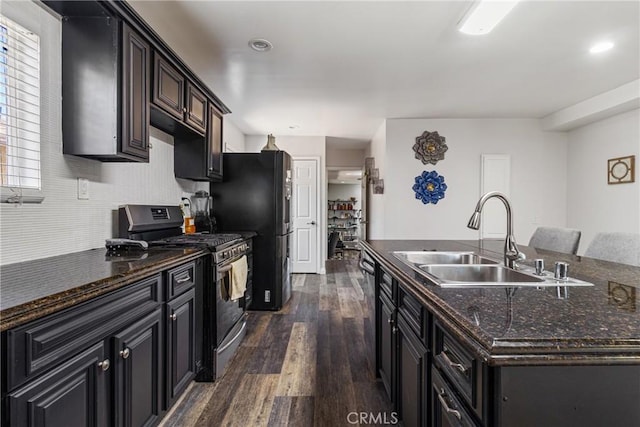 kitchen with gas stove, black fridge, a kitchen island with sink, dark wood-type flooring, and a sink