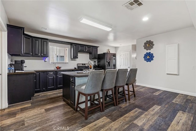 kitchen featuring a kitchen breakfast bar, an island with sink, dark wood-type flooring, visible vents, and appliances with stainless steel finishes