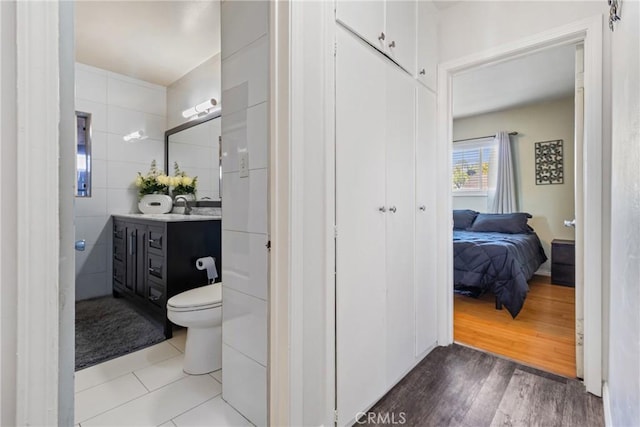 ensuite bathroom with ensuite bathroom, vanity, toilet, wood finished floors, and tile walls