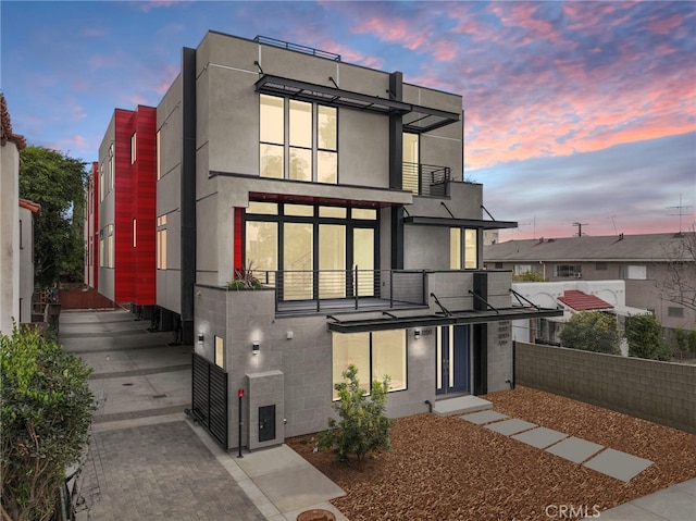 back of house featuring fence, a balcony, concrete block siding, and stucco siding
