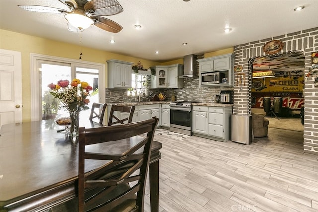 610 Woodington Dr, Lancaster, CA 93535 - kitchen with appliances with stainless steel finishes, wall chimney range hood, ceiling fan, gray cabinetry, and tasteful backsplash