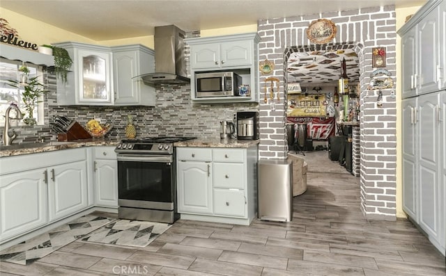 610 Woodington Dr, Lancaster, CA 93535 - kitchen featuring stainless steel appliances, wall chimney exhaust hood, a sink, light stone counters, and wood finish floors