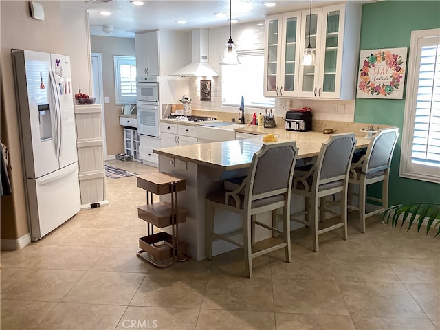 23796 Corte Picante, Murrieta, CA 92562 - kitchen featuring glass insert cabinets, wall chimney exhaust hood, white appliances, a peninsula, and white cabinetry