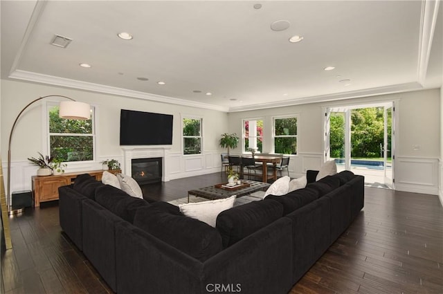 living area with dark wood finished floors, a decorative wall, crown molding, and visible vents