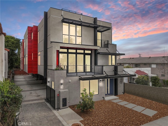 back of house with concrete block siding, fence, stucco siding, and a balcony