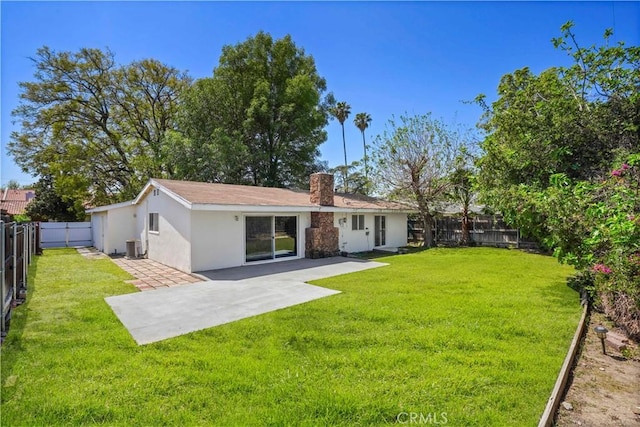 rear view of house featuring stucco siding, a chimney, a patio area, a fenced backyard, and a lawn