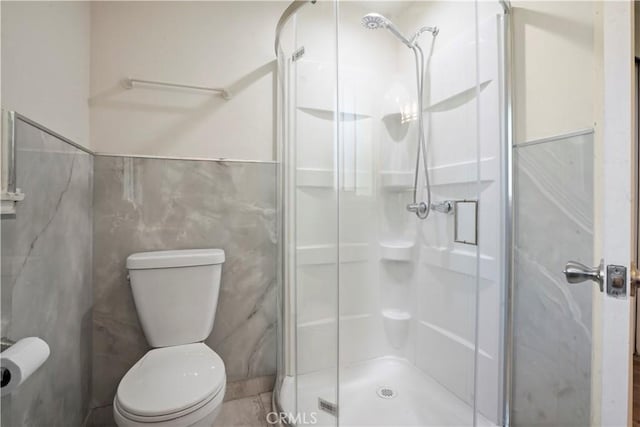 bathroom featuring tile walls, toilet, a stall shower, and wainscoting