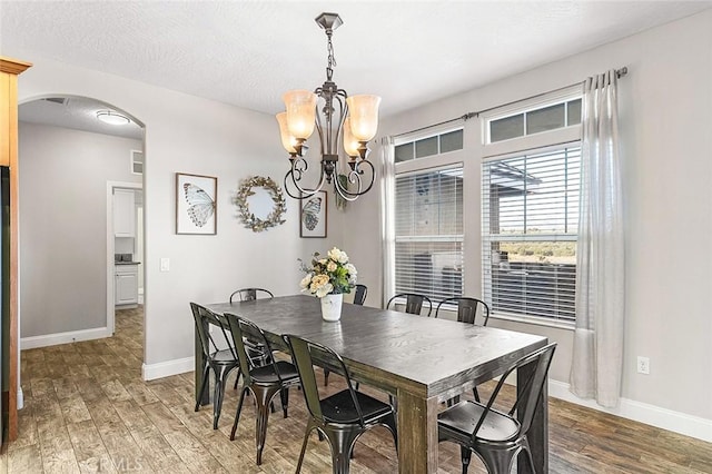 7922 Los Palmas Dr, Oak Hills, CA 92344 - dining space featuring baseboards, an inviting chandelier, a textured ceiling, arched walkways, and wood finished floors