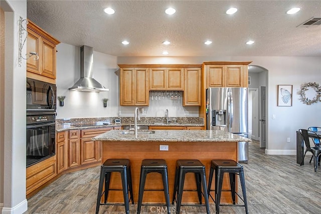 7922 Los Palmas Dr, Oak Hills, CA 92344 - kitchen featuring a sink, black appliances, wall chimney exhaust hood, and an island with sink