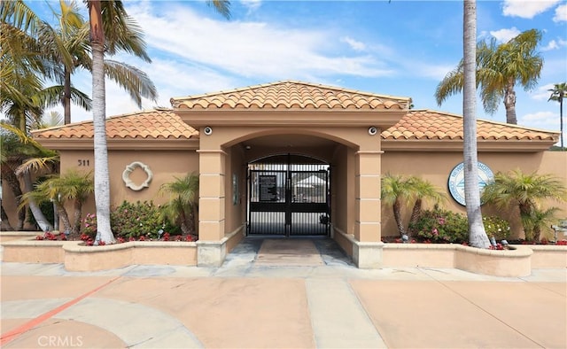 view of exterior entry with stucco siding, a tiled roof, and a gate