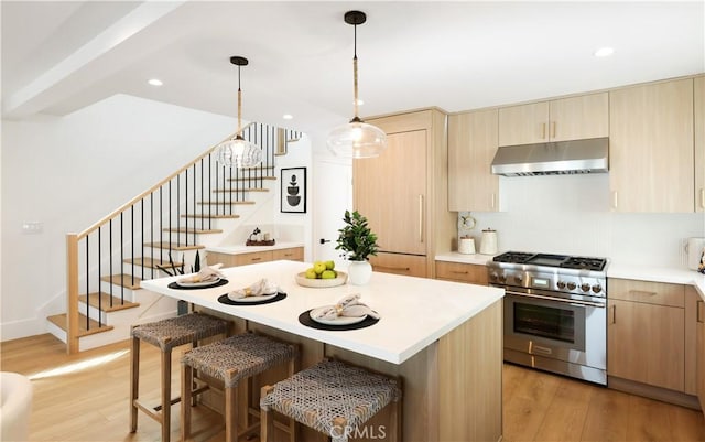 kitchen with stainless steel range, light countertops, under cabinet range hood, and light wood-type flooring