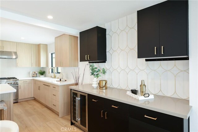 kitchen featuring dark cabinets, light brown cabinetry, under cabinet range hood, high end stove, and wine cooler