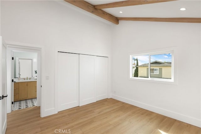 unfurnished bedroom with light wood finished floors, a sink, lofted ceiling with beams, a closet, and baseboards