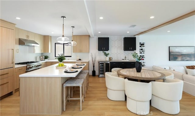 kitchen featuring beverage cooler, light brown cabinets, stainless steel stove, under cabinet range hood, and open floor plan