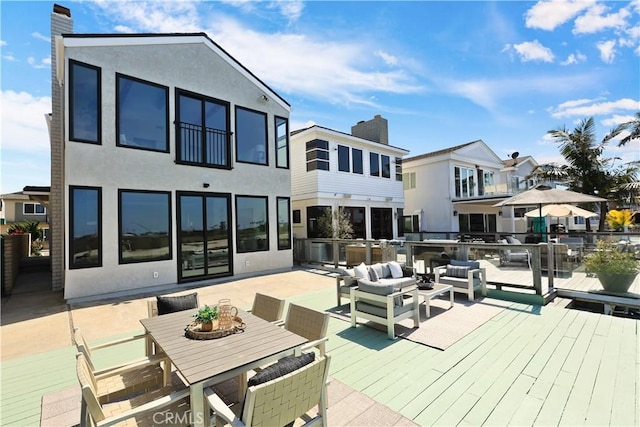 rear view of property featuring a deck, outdoor dining space, stucco siding, and a chimney