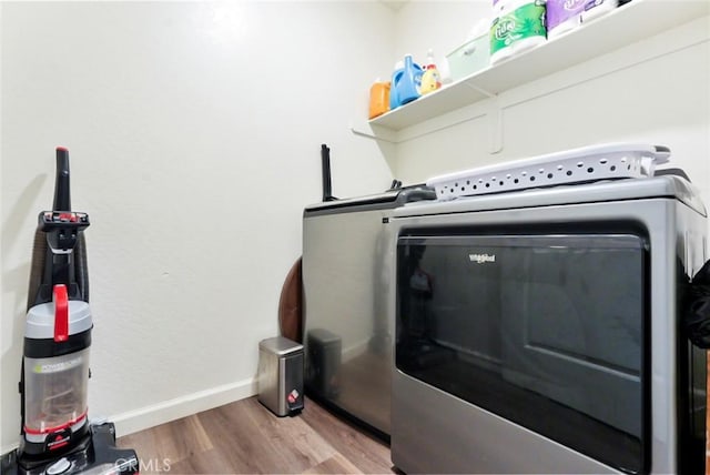 clothes washing area with washing machine and clothes dryer, wood finished floors, laundry area, and baseboards