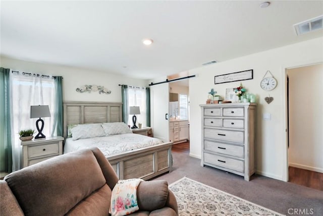 carpeted bedroom featuring a barn door, visible vents, and baseboards