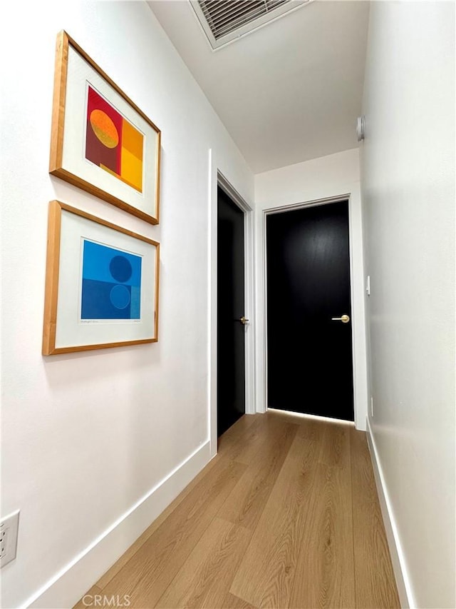 hall with visible vents, baseboards, and wood finished floors