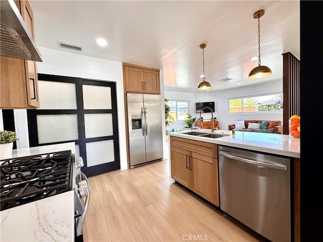 kitchen featuring under cabinet range hood, visible vents, appliances with stainless steel finishes, light wood finished floors, and pendant lighting