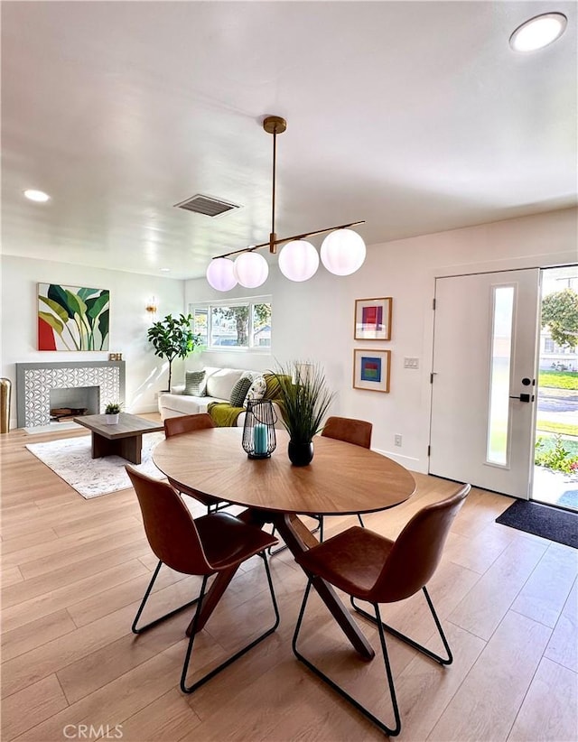 dining room with light wood-type flooring, visible vents, recessed lighting, a tile fireplace, and baseboards