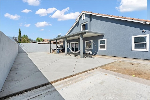 rear view of house featuring a tiled roof, a fenced backyard, a patio, and stucco siding