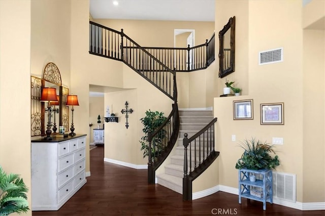 stairs with baseboards, visible vents, a towering ceiling, and wood finished floors