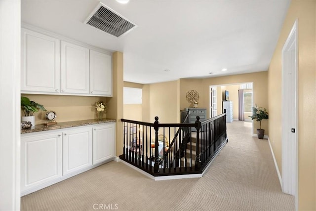 corridor with visible vents, an upstairs landing, baseboards, and light carpet