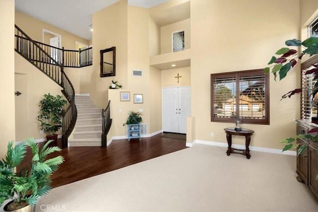 carpeted foyer with stairway, baseboards, visible vents, and a high ceiling