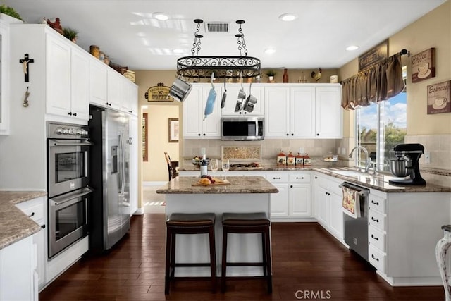 kitchen with a sink, visible vents, white cabinets, a kitchen island, and appliances with stainless steel finishes
