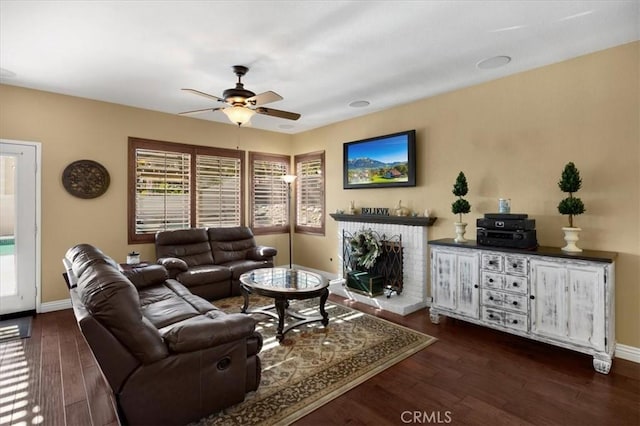 living room featuring a brick fireplace, baseboards, a ceiling fan, and dark wood-type flooring