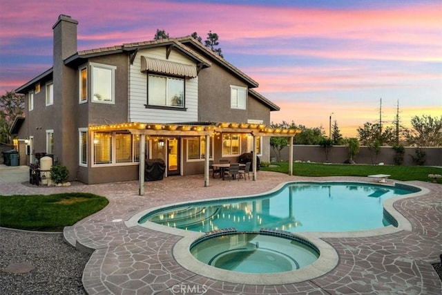 back of property at dusk with stucco siding, a pool with connected hot tub, a chimney, a pergola, and a patio area