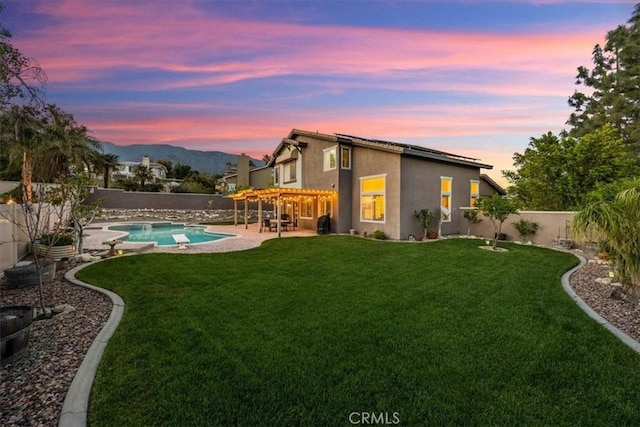 rear view of property featuring a yard, a mountain view, stucco siding, and a fenced backyard
