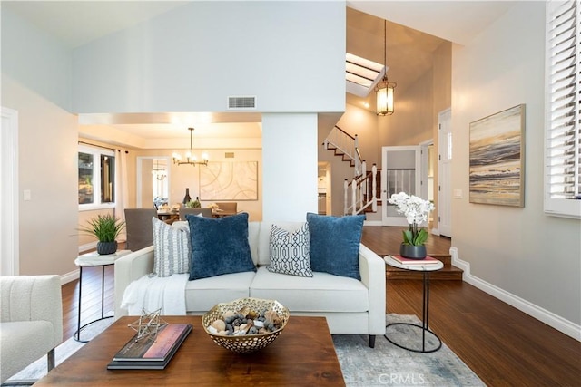 living area featuring a chandelier, stairway, baseboards, and wood finished floors