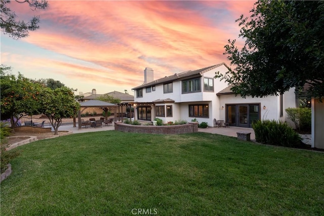 back of house at dusk with a patio area, a gazebo, stucco siding, and a lawn