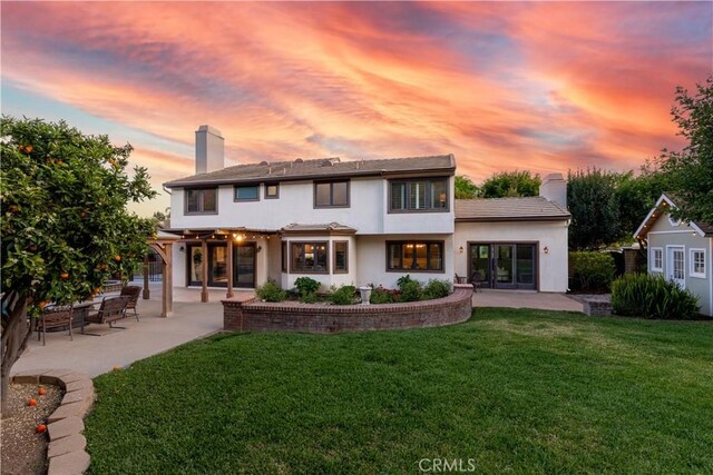 back of property with a patio area, a yard, a chimney, and stucco siding