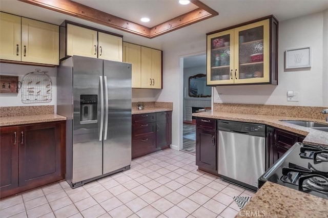 kitchen featuring a tray ceiling, a sink, light tile patterned flooring, glass insert cabinets, and appliances with stainless steel finishes