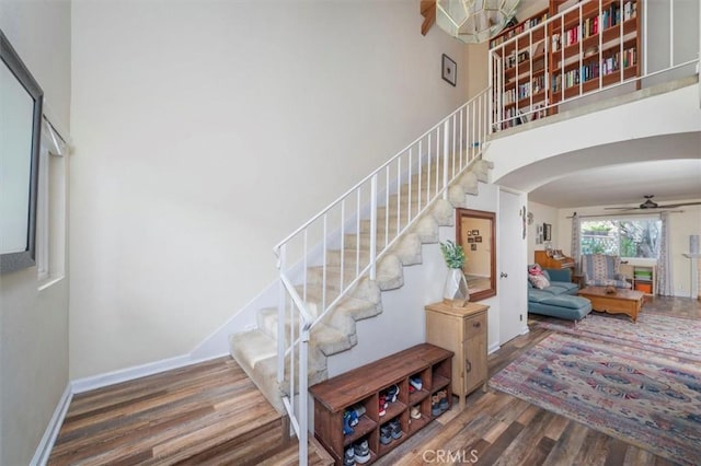 stairway featuring arched walkways, baseboards, a ceiling fan, a high ceiling, and wood finished floors