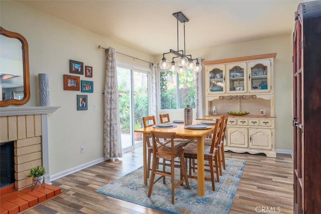 dining space featuring baseboards, a brick fireplace, and wood finished floors