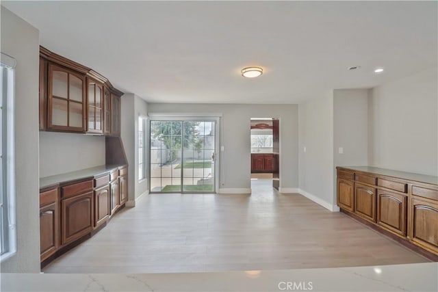 kitchen with light wood finished floors, glass insert cabinets, baseboards, and light countertops