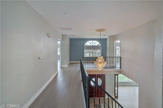 corridor with wood finished floors, visible vents, baseboards, and an upstairs landing