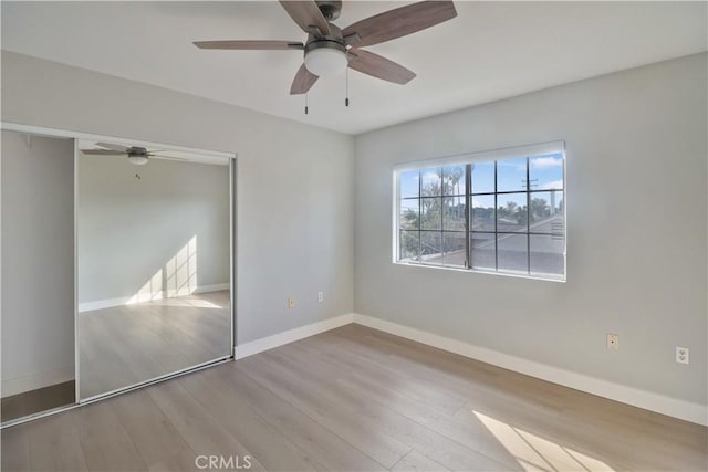 unfurnished bedroom featuring wood finished floors, a closet, a ceiling fan, and baseboards