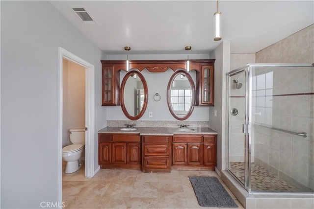 full bathroom with double vanity, a stall shower, toilet, visible vents, and a sink
