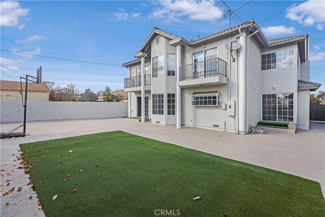 back of house with stucco siding, a lawn, a patio, fence, and a balcony