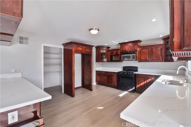 kitchen with stainless steel microwave, black gas stove, glass insert cabinets, visible vents, and a sink