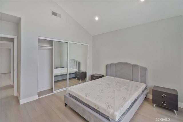 bedroom featuring visible vents, baseboards, a closet, light wood-type flooring, and high vaulted ceiling