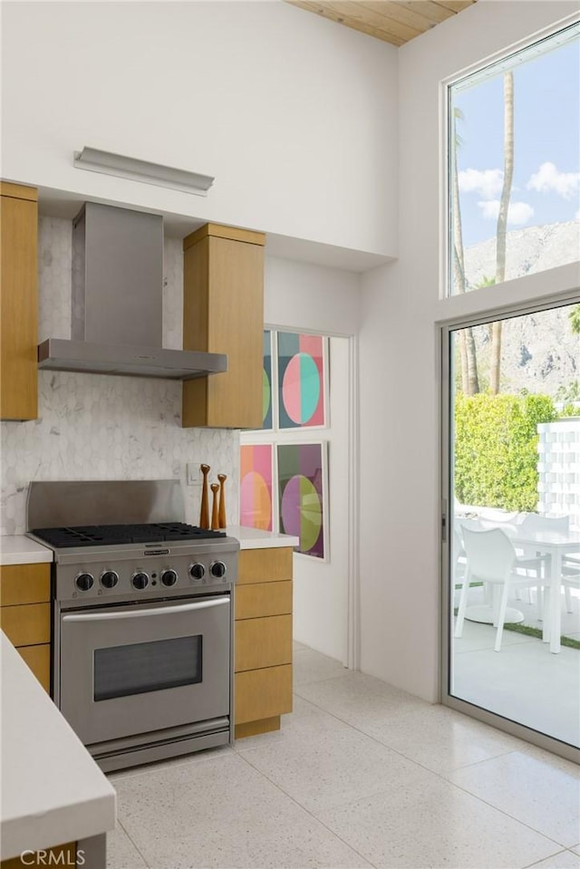 kitchen featuring light countertops, light speckled floor, stainless steel gas range oven, and wall chimney range hood