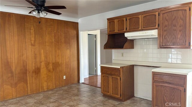 432 Oakford Dr, Los Angeles, CA 90022 - kitchen featuring under cabinet range hood, tasteful backsplash, a ceiling fan, brown cabinets, and wooden walls