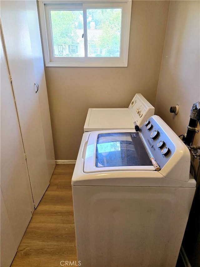 clothes washing area featuring laundry area, light wood-style flooring, plenty of natural light, and washing machine and clothes dryer
